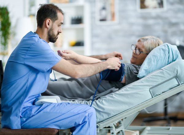 male-caretaker-in-a-nursing-home-taking-bood-press-STRR45L-1-scaled.jpg