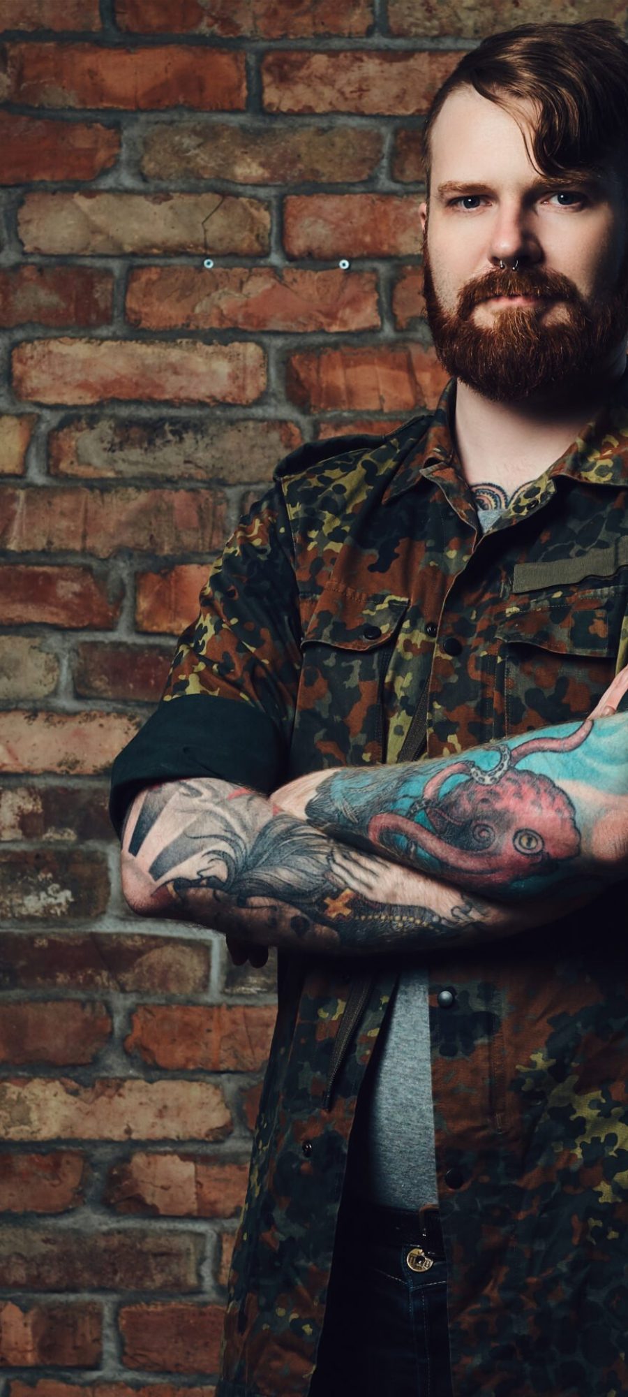 portrait-redhead-bearded-male-with-tattoos-arms-dressed-military-jacket-wall-brick-scaled.jpg