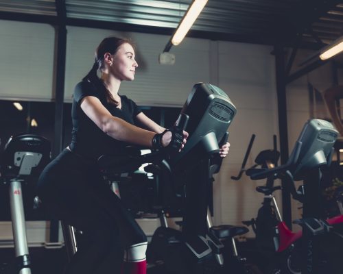 side-view-young-woman-riding-exercise-bike-gym-scaled.jpg