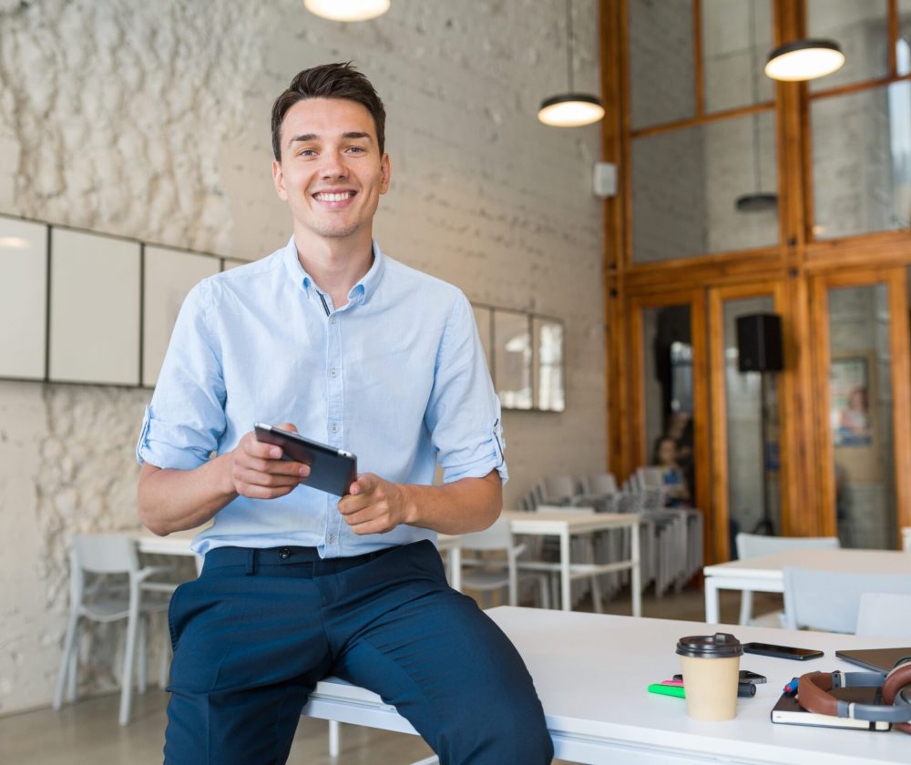 young-stylish-smiling-man-co-working-office-startup-freelancer-holding-using-tablet-scaled.jpg